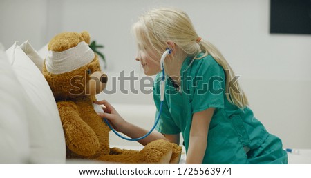 Cute little girl wearing doctor suit playing at home, performing a medical check-up her teddy bear