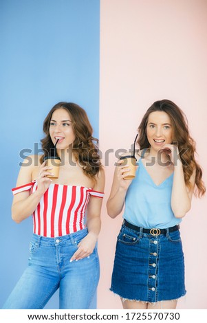 Image of two happy women holding takeaway coffee in paper cups isolated over color background