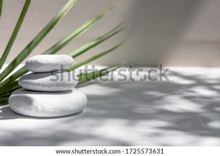 Three grey roundstones and bath towels on white background with green leaves. Spa stones, zen like concept.