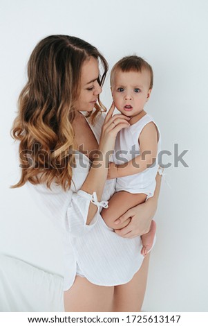 Mom with the baby on the bed in a bright room, a gentle hug, Mom kisses her son, kisses her legs, the child bites her mother, mom and baby laugh