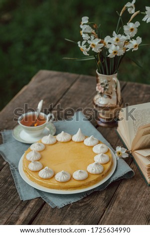 Lemon cake with meringues on a wooden garden table with white narcissus flowers and book