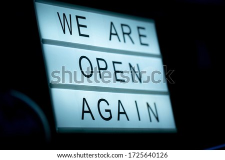 Lightbox with a sign we are open again behind a glass door of the cafe in the evening. We're open again after quarantine, photo of small business owner. Please wear a face mask and keep your distance