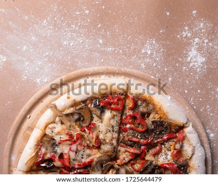 Pizza on a wooden tray with flour, tomatoes, meat, mushrooms.