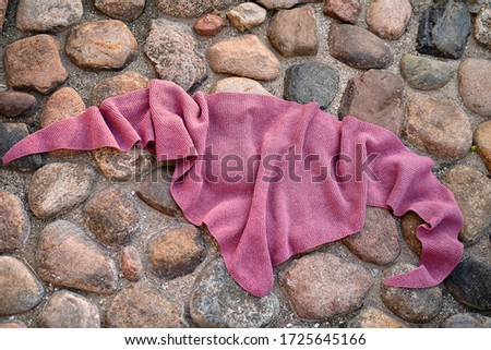 on the ground covered with stones lies a triangular knitted shawl