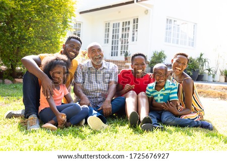Three generation African American family spending time in their garden on a sunny day, sitting on a lawn and smiling.
