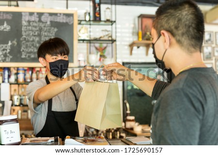 Social distance conceptual waiter giving takeaway bag to customer at cafe. Royalty-Free Stock Photo #1725690157