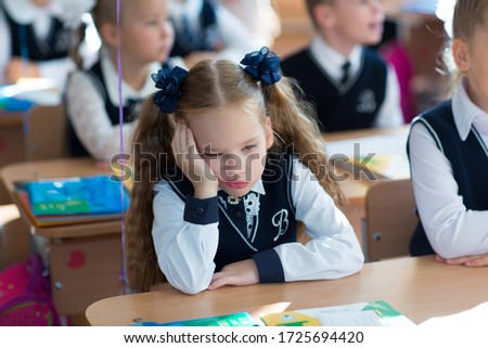 Girl student first grader at school tired of learning tired of learning sitting at her desk in a class of suffering sadness hopelessness 1st grade Royalty-Free Stock Photo #1725694420
