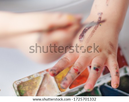 
Kid is paintning on his hands. Colorful paints.