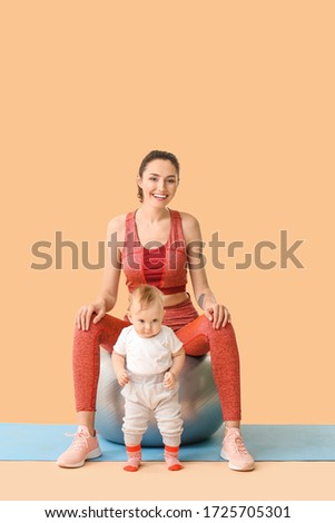 Young sporty mother and her baby doing exercises with fitball on color background