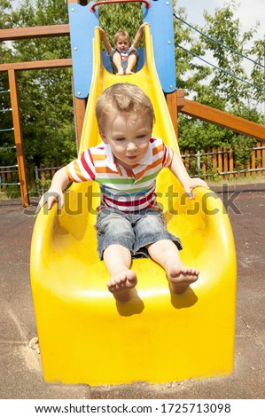 Twin brothers playing on yellow slide in playground
