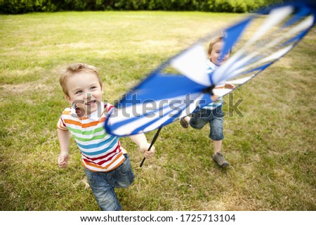 Twin brothers running in park holding paper windmill