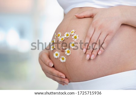 Pregnant woman wearing flowers in heart shape on belly, close up
