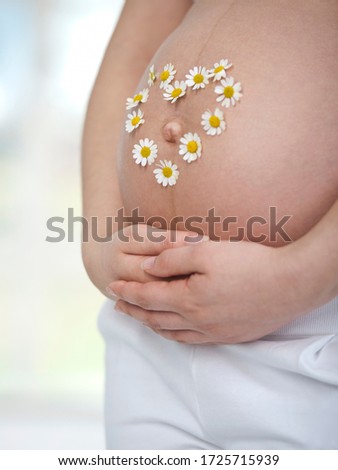 Pregnant woman wearing flowers in heart shape on belly, close up