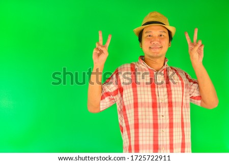 Smiling Asian man with wears straw hat and showing peace sign on over green screen background.