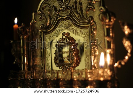 Chanukah oil candle on a silver menorah with one candle lit. The Hebrew text says these candles are sacred