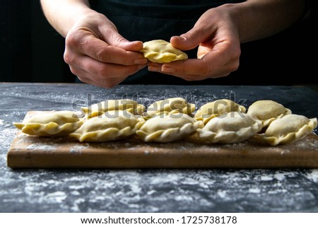 Cook in a dark jacket prepares dumplings. over a dark table on which the finished dumplings are laid out. Front views, close-up.