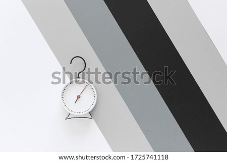 Time. Alarm clock with a dial with one red arrow and a hook in the shape of a question mark. Background gray, white, black stripes. Top view.  Copy space. 