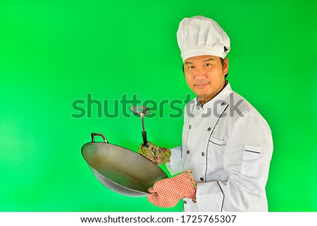 Young chef holding a pan with the spatula on over green screen background.