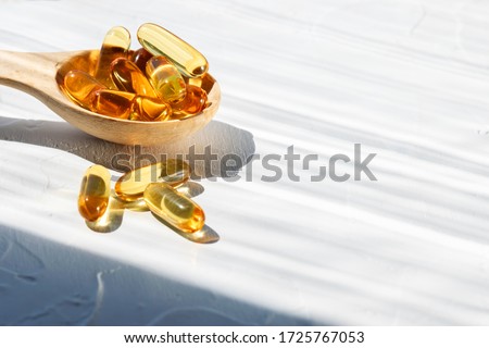 Omega 3 capsules in the wooden spoon on white concrete background, hard shadows, copy space for your design. Cod liver oil capsules on the table. Healthy life style concept.