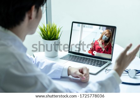 Asian doctor man wearing stethoscope and ground white coat using video call with woman in modern hospital.