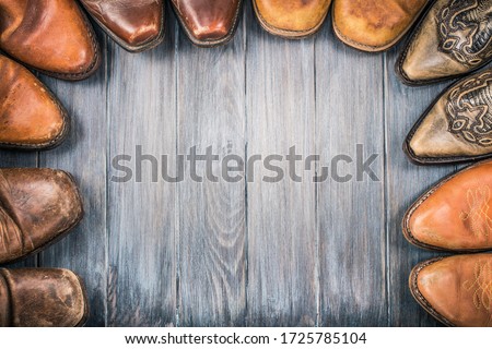 Old retro leather cowboy boots on aged textured wooden floor for background. Wild West nostalgic concept. Vintage style filtered photo