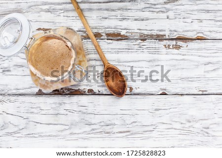 Active live whole wheat sourdough starter with a wooden spoon over a white rustic wood table  background with free space for text Image shot from overhead view.