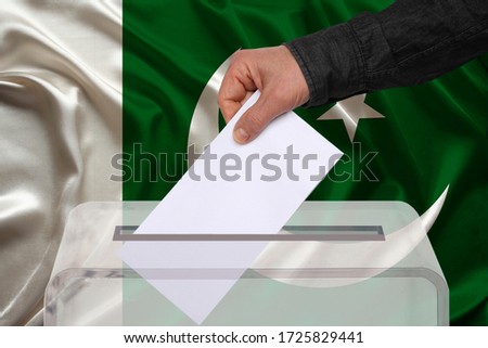 male voter drops a ballot in a transparent ballot box against the background of the national flag of Pakistan, concept of state elections, referendum
