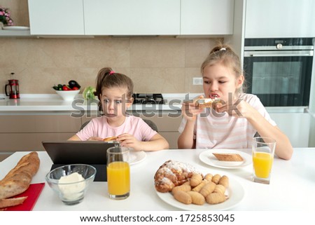 Two sisters having breakfast and watching cartoons on tablet together, happy family concept