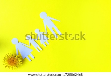 Silhouette of a family with two children made of paper on a yellow background with a dandelion flower.
