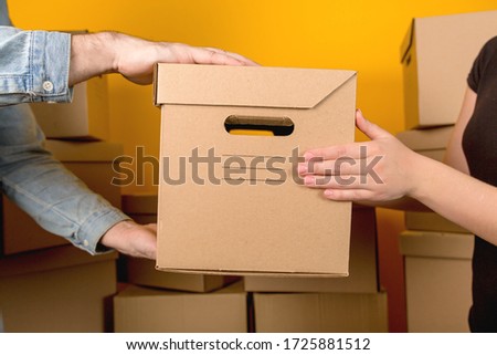 Delivery man handing the customer a cardboard box with a parcel close up on a yellow background Royalty-Free Stock Photo #1725881512