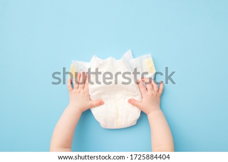 Baby hands touching white diaper on light blue table background. Pastel color. Closeup. Point of view shot. Royalty-Free Stock Photo #1725884404