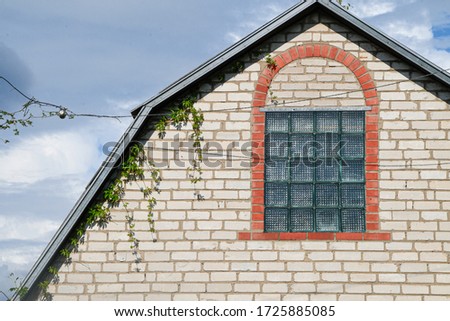 A picture of the part of the barn rooftop and window made of glass blocks framed in silicate brick arch dark clouds on the background