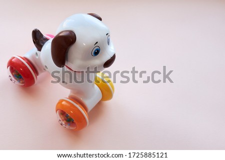 Children's toy from plastic a white dog with brown ears and a tail, on wheels on a pink background. Flat lay. Copy space.
