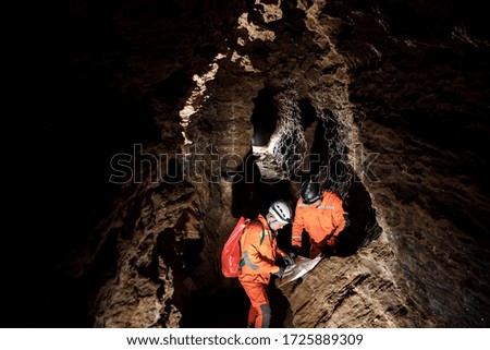 Two men, strong physique, explore the cave. Men dressed in special clothes to pass through the cave and stopped, looking at the map. Royalty-Free Stock Photo #1725889309