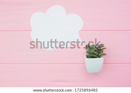 Close-up view of white blank speech bubble with green plant in pot on pink wooden background