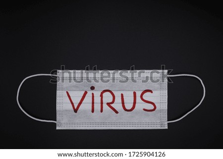 Surgical mask seen from above with virus sign written in red on a black background. Basic medical equipment.