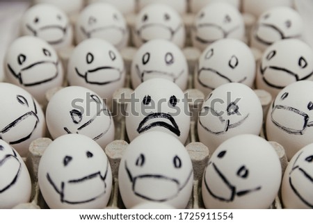 White eggs with faces drawn arranged in carton. emoticons drawn with a black marker. sad face against the background of masked eggs coronovirus pandemic