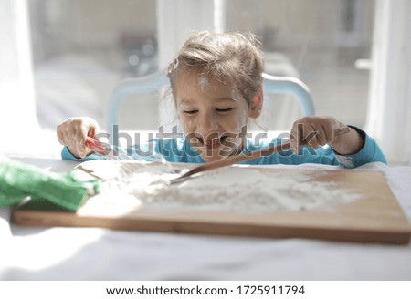 A selective focus shot of a girl child playing with flour powder at the kitchen