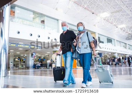 couple of two seniors or mature people walking in the airport going to their gate and take their flight wearing medical mask to prevent virus like coronavirus or covid-19 - carrying luggage or trolley Royalty-Free Stock Photo #1725913618
