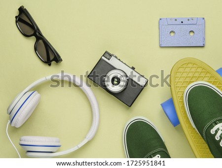 Hipster outfit. Skateboard with headphones, audio cassette, retro camera and sneakers on green pastel background. Creative fashion minimalism. Minimal summer fun. Top view