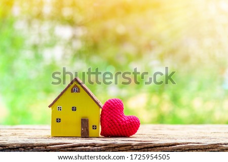 Yellow house model and red heart put on the wood on sunlight in the public park, The buying a new real estate as a gift to family or the one loved concept.