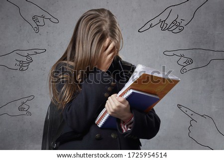 young lonely teenage girl crying on studio isolated grey background with drawings of pointing fingers symbolizing harassment