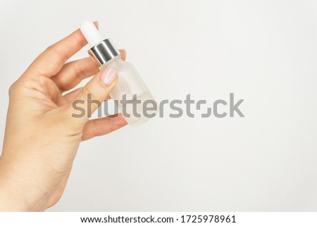Transparent and matt bottle with serum or oil in glass bottle and pipette . Skincare beauty product in hand on the white background. Glass eye dropper bottle, wellness and self care for lash, eyebrow