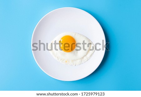 Breakfast, fried egg, yolk, omelet on white plate with color table, creative picture