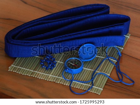Blue belt for karate, a plastic water compass, an elastic band for hair, a Makisu rug on a wooden background.