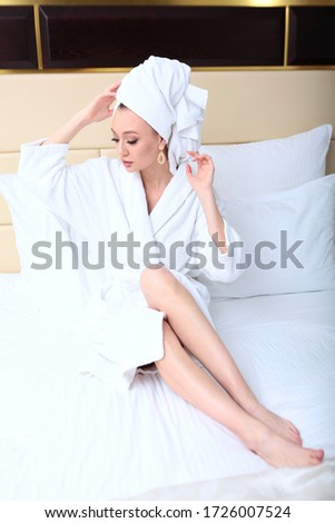 A girl in a Bathrobe and a towel on her head is resting on a bed in a hotel room. Concept of travel and recreation.