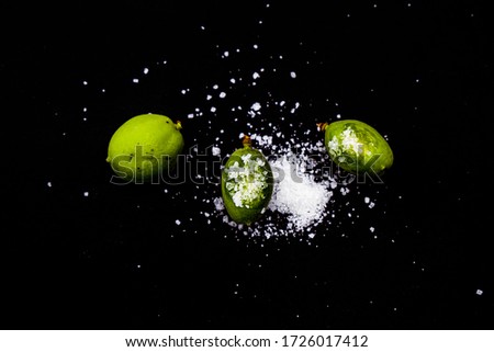 Green unripe apricot fruits with white salt on a black background.