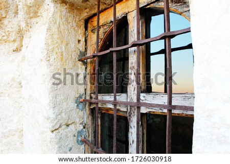Rustic wooden window in the stone wall with iron grid