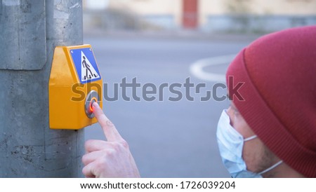 protection against coronavirus on street, young man in medical mask and rubber gloves disinfects pedestrian crossing button at traffic light with antiseptic and presses it close-up