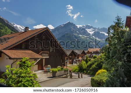 Amazing view of the snowy mountain peaks of the Swiss Alps from the small resort village of Champery in Switzerland. Bright blue sky and white fluffy clouds over rocky peaks. Chalets along the road.